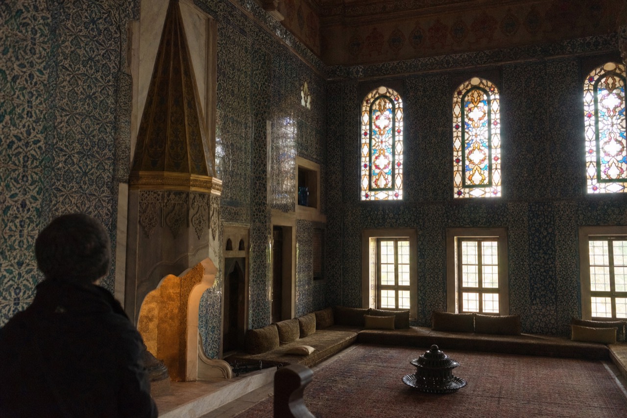Iznik-tiled hall inside the Topkapi Palace Harem with stained-glass windows and a marble fireplace