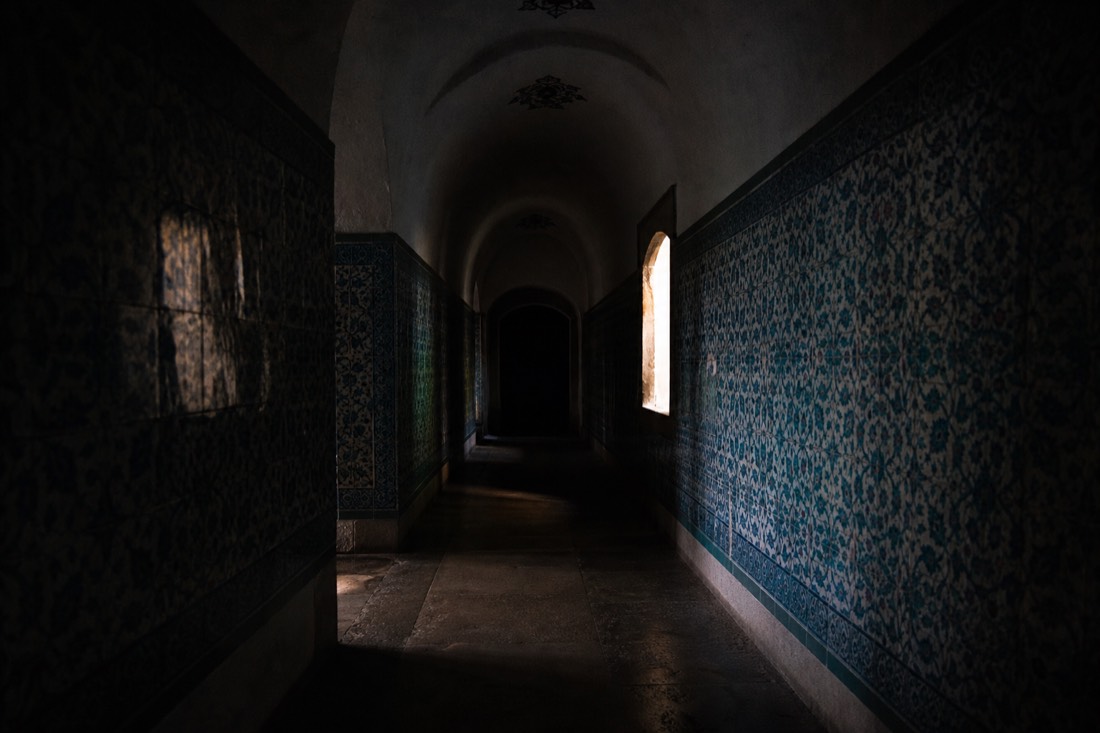 Arched tiled corridor of the Topkapi Palace Harem receding into shadow with a single window glow