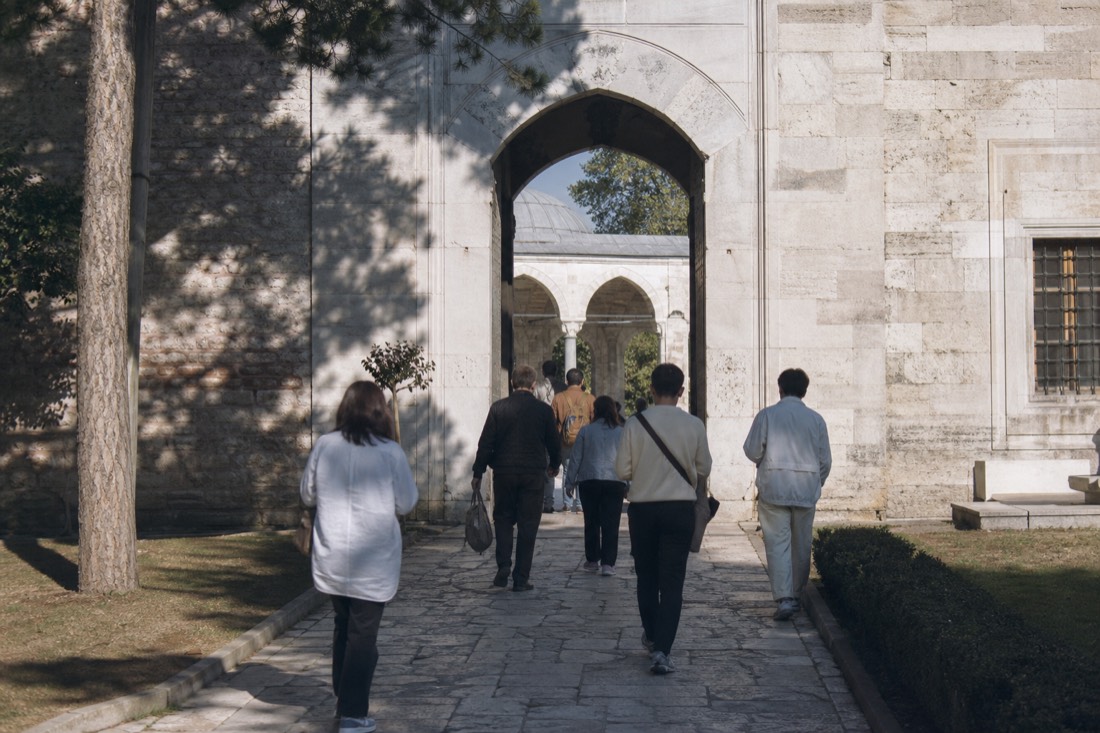 Visitors from behind at a stone gateway between Topkapi Palace courtyards on a bright day
