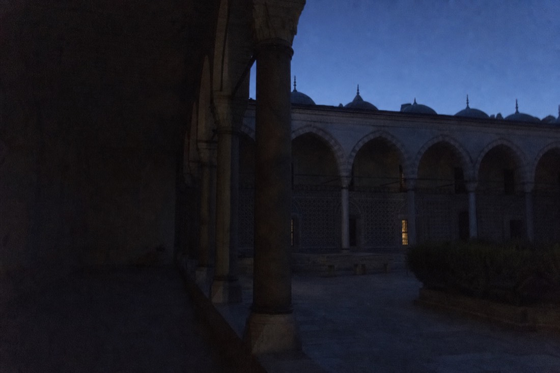 Shadowed arcaded courtyard corner of Topkapi Palace at dusk with a single lit window